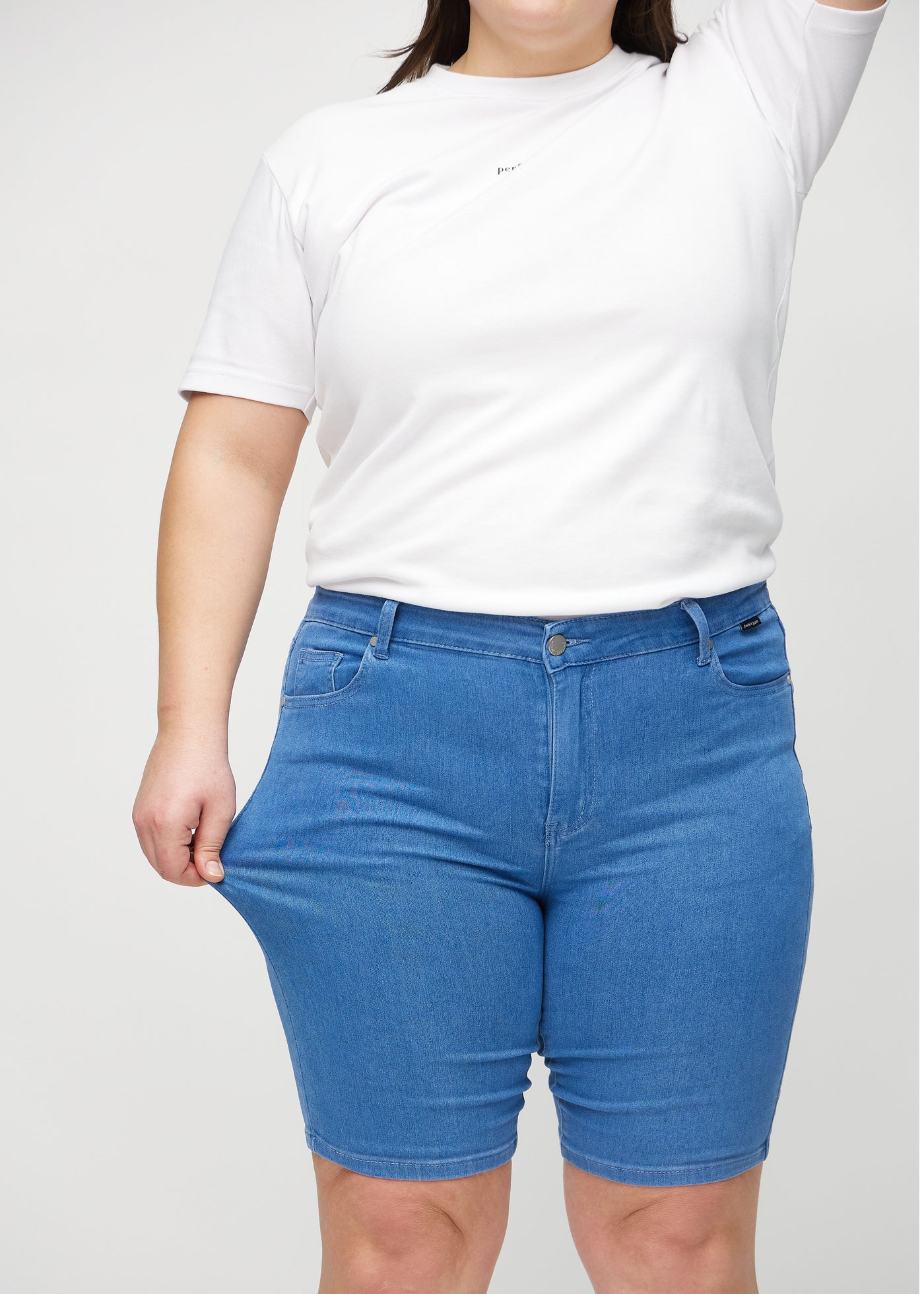 Plus-size model strækker shortsene ved låret for at vise stretch.