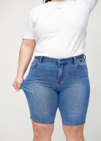 Plus-size model strækker shortsene ved låret for at vise stretch.