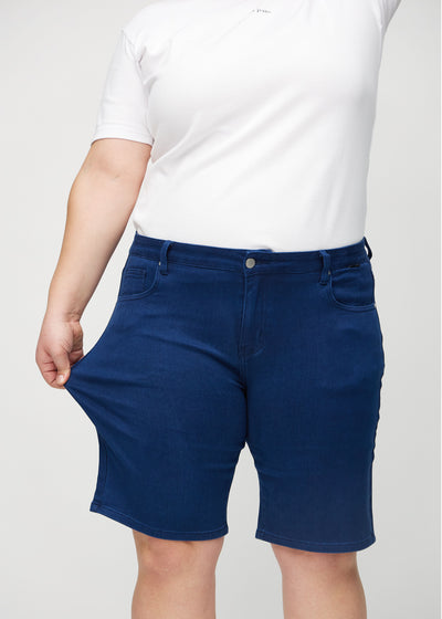 Plus-size model strækker shortsene ved låret for at vise stretch.