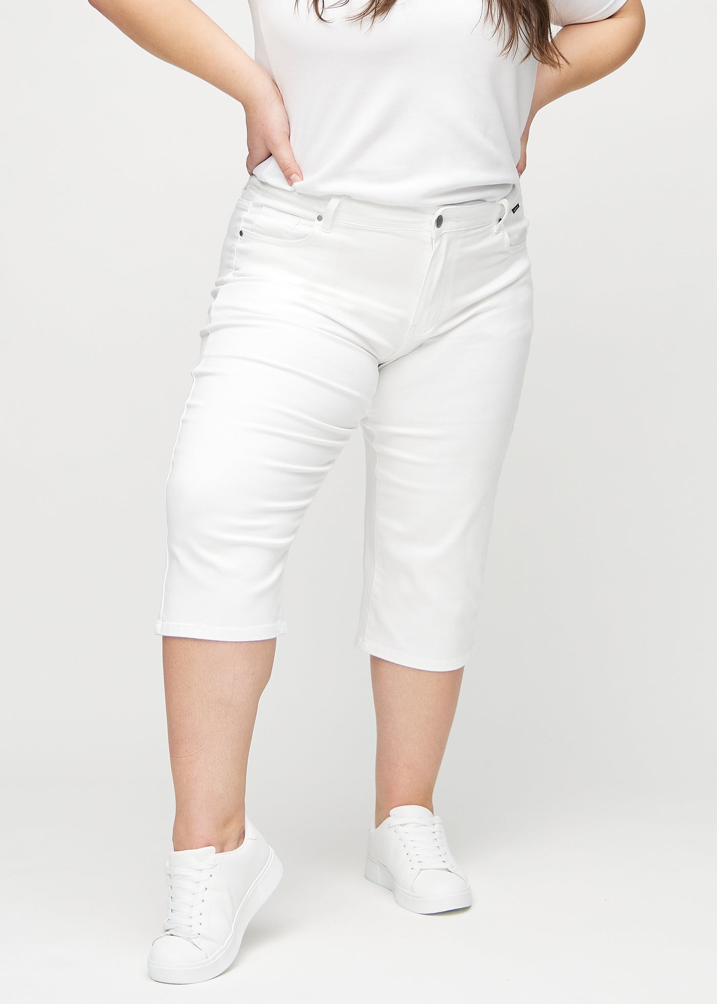 Hvide regular capris, modelnavn Marguerites, som sidder lige til benet og slutter lige under knæet på en plus-size model, set forfra.