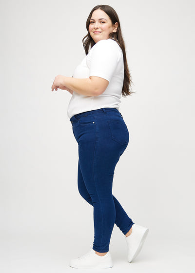 Mørkeblå skinny jeans set fra siden på en plus-size model.