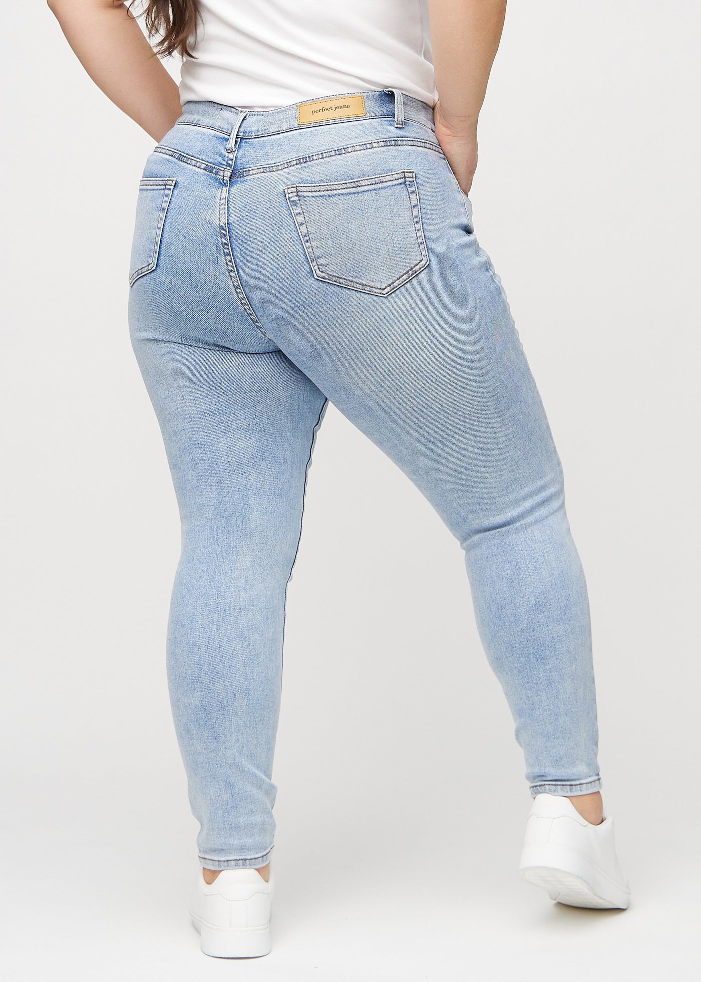 Lys denim skinny jeans set bagfra på en plus-size model, så man kan se hele produktet.