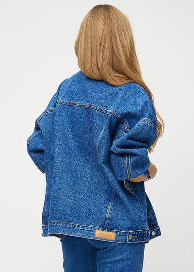 Kvindelig model i mørkeblå denim jakke, set bagfra, fremhæver detaljerne på ryggen i farven Oceans.
