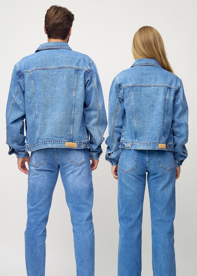 Unisex blå denim jakke set bagfra på mand og kvinde, viser rygdetaljer og højkvalitetssømme.
